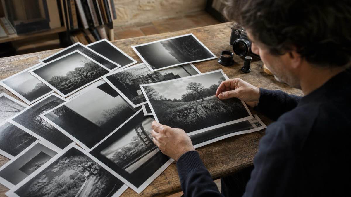 Un photographe sélectionne des tirages noir et blanc sur une table en bois